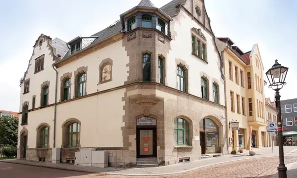 Historisches Stadthaus mit Jugendstilfassade und grünen Fenstern in einer Altstadtstraße.