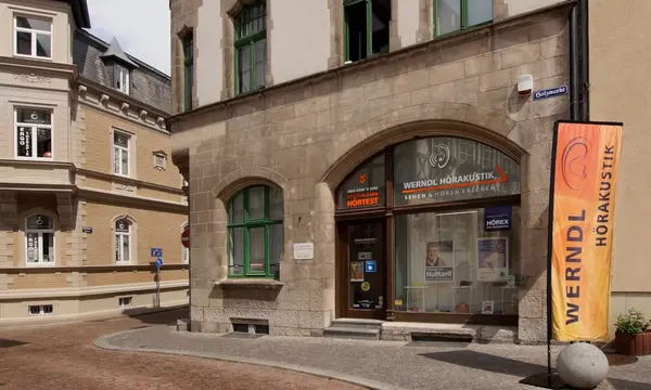 Das Bild zeigt das Geschäft von Werndl Hörakustik mit orangefarbener Werbefahne am Eingang.