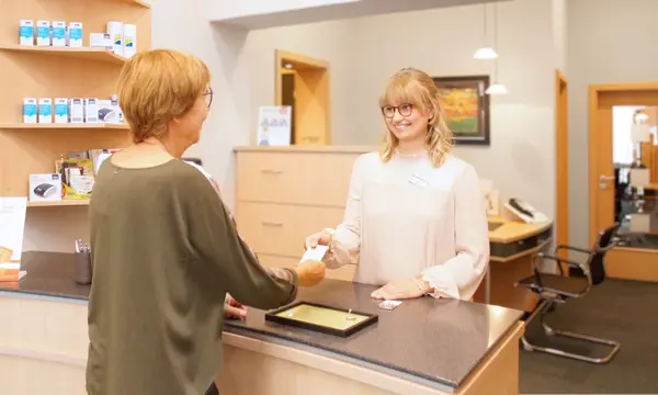 Freundliche Mitarbeiterin am Empfang einer modernen Hörakustik-Filiale berät Kundin.