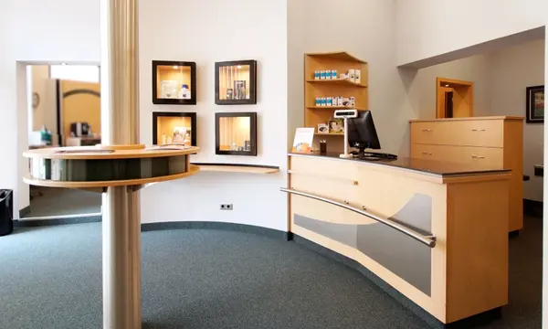 Moderner Empfangsbereich einer Arztpraxis mit Computer, Holztheke und Wartebereich.